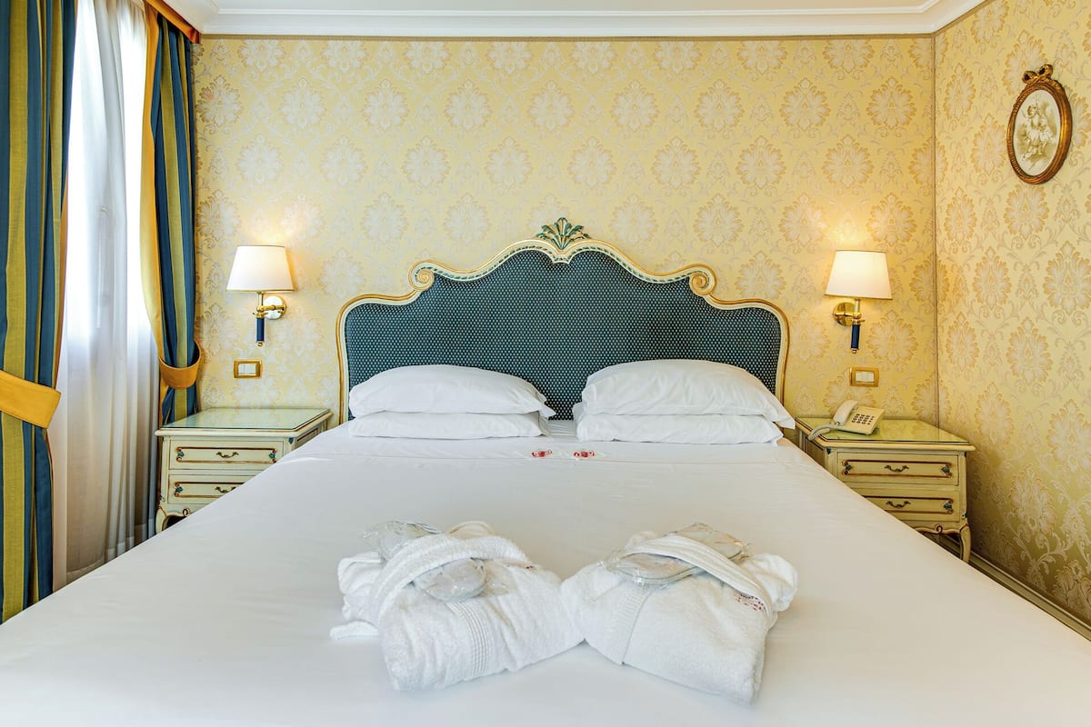 Ein Hotelzimmer mit einem großen Bett, zwei Nachttischen, einem Wandtelefon und einer Ablagefläche.