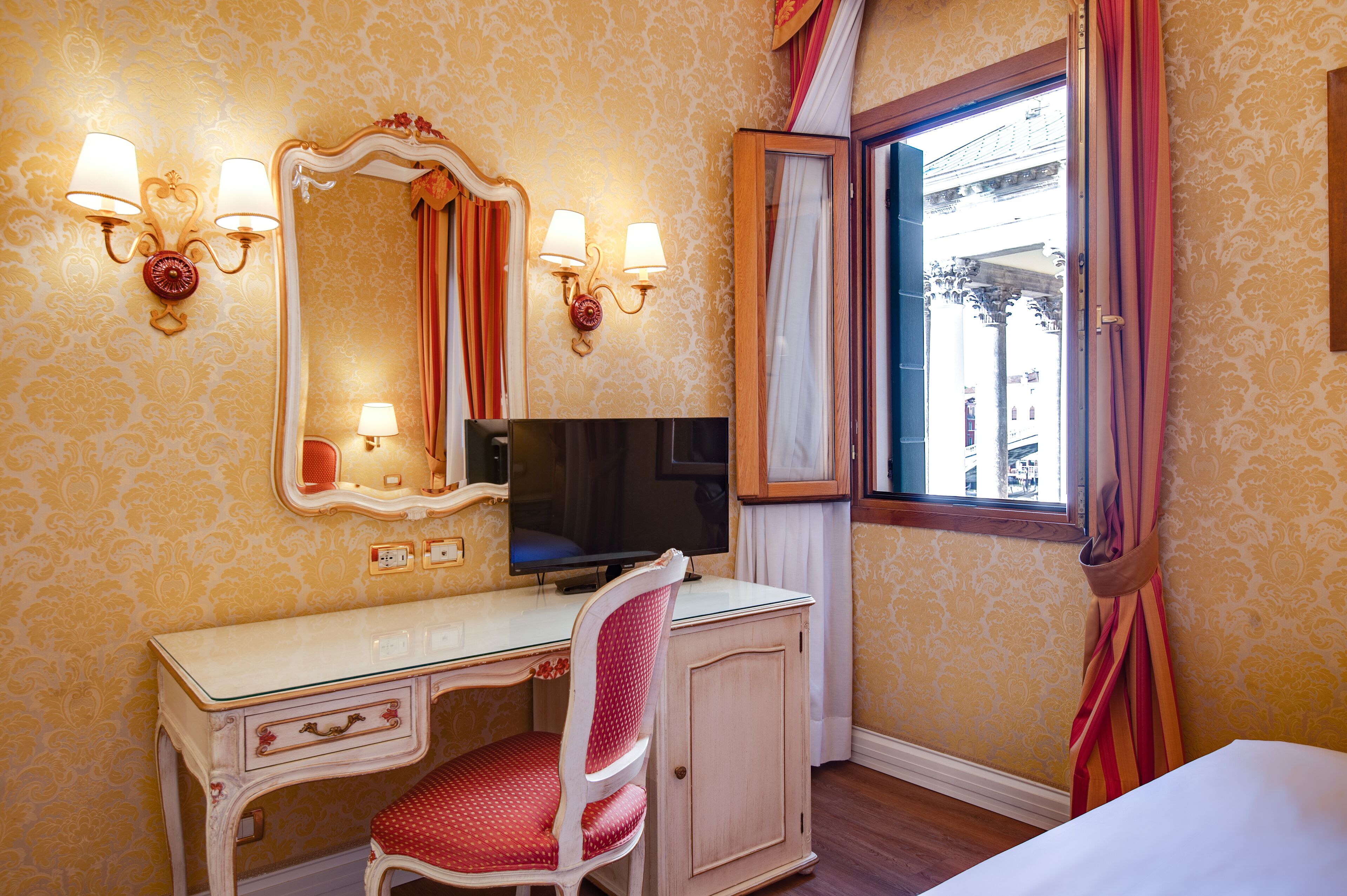 A hotel room with a desk, chair, television, and a window with curtains.