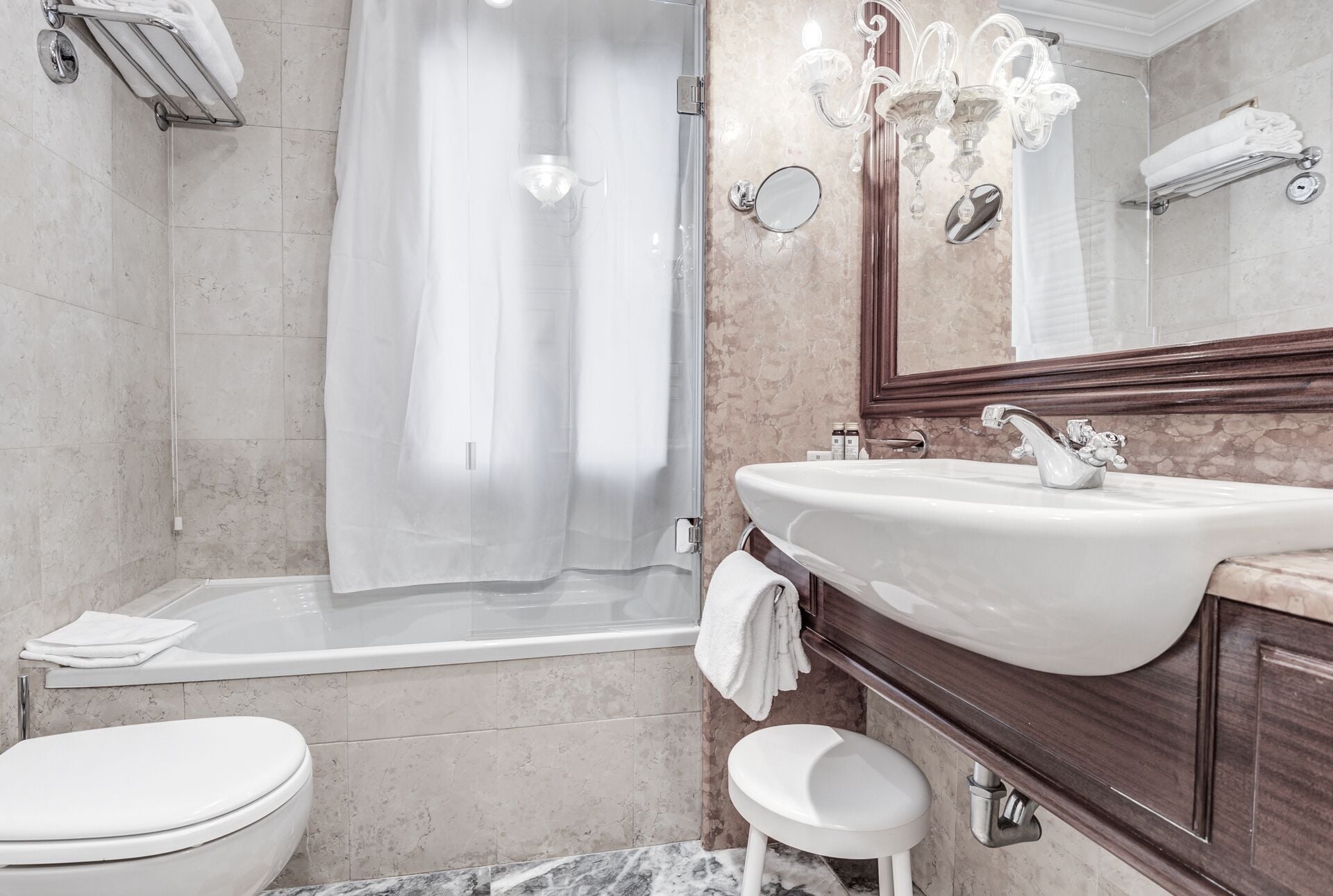 A modern bathroom with a glass shower enclosure, a white sink with a decorative faucet, and a marble-tiled floor.