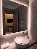 Un bagno moderno con uno specchio grande, un lavabo rotondo e un water visibile sullo sfondo.