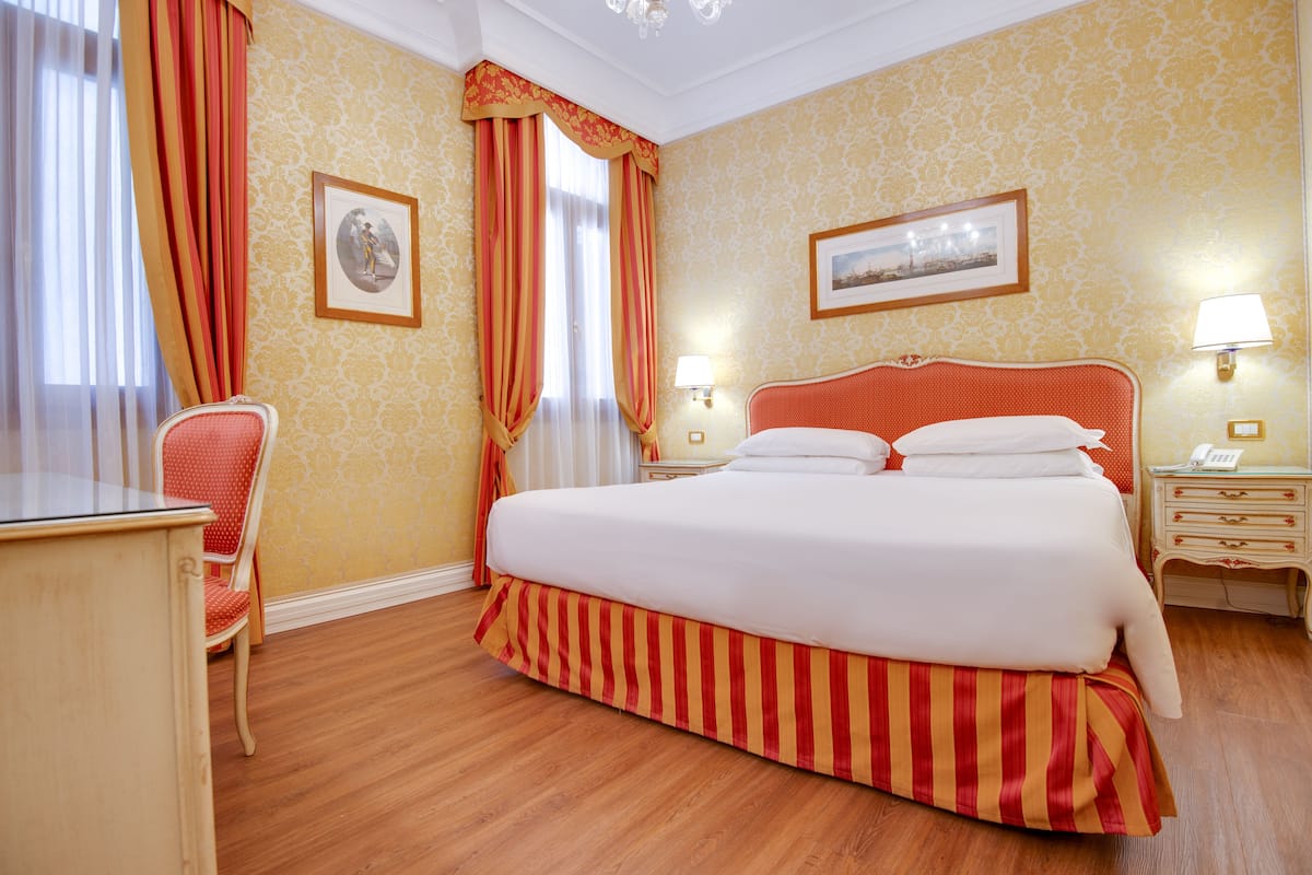 Ein Hotelzimmer mit einem großen Bett, einem Schreibtisch, einem Stuhl und zwei Nachttischlampen.