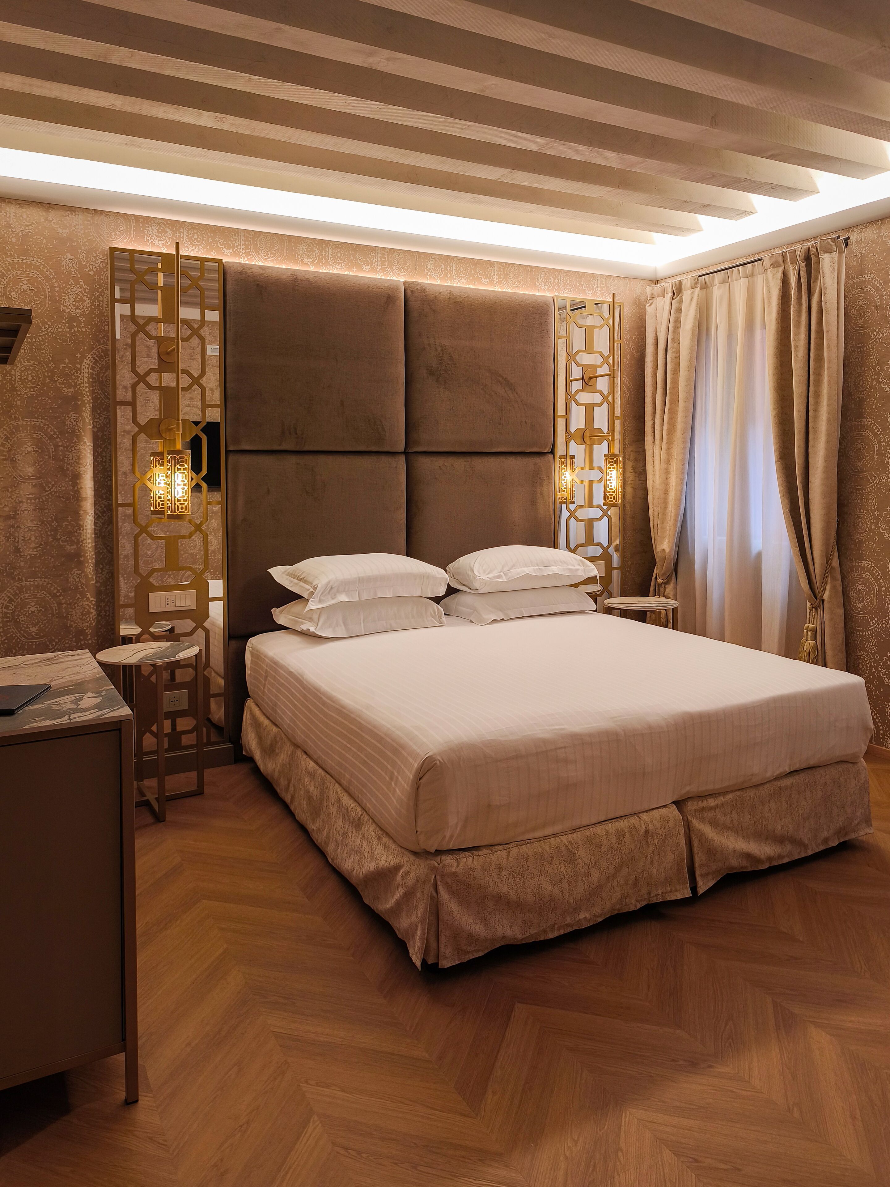 A bedroom with a large bed, a bedside table, a small table, and a decorative wall panel.