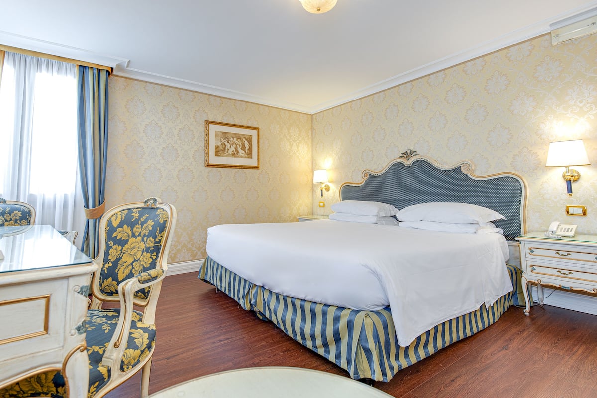 Ein Hotelzimmer mit einem großen Bett, einem Schreibtisch mit Stuhl, einem Nachttisch und einer Wandlampe.