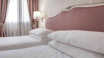 A hotel room with a large bed, two pillows, a nightstand with a lamp, and a window with curtains.