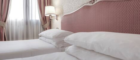 Een hotelkamer met een groot bed, twee kussens, een nachtkastje met een lamp en een raam met gordijnen.