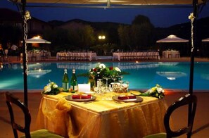 An outdoor dining area with a pool view, covered by a canopy, and tables set for a meal. - Borgo degli Olivi (Piombino)