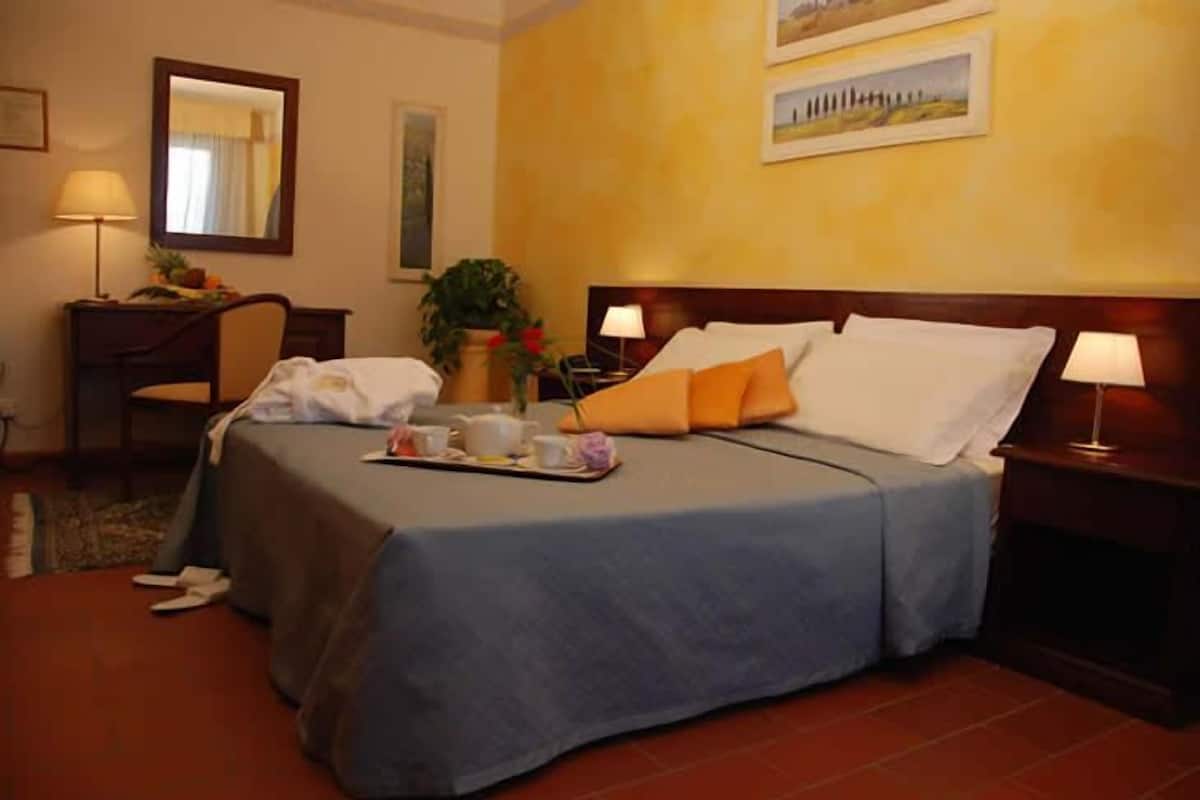 Une chambre d’hôtel comprenant un lit, des tables de chevet, un bureau, une chaise et une table à manger mise avec des éléments pour le petit-déjeuner.