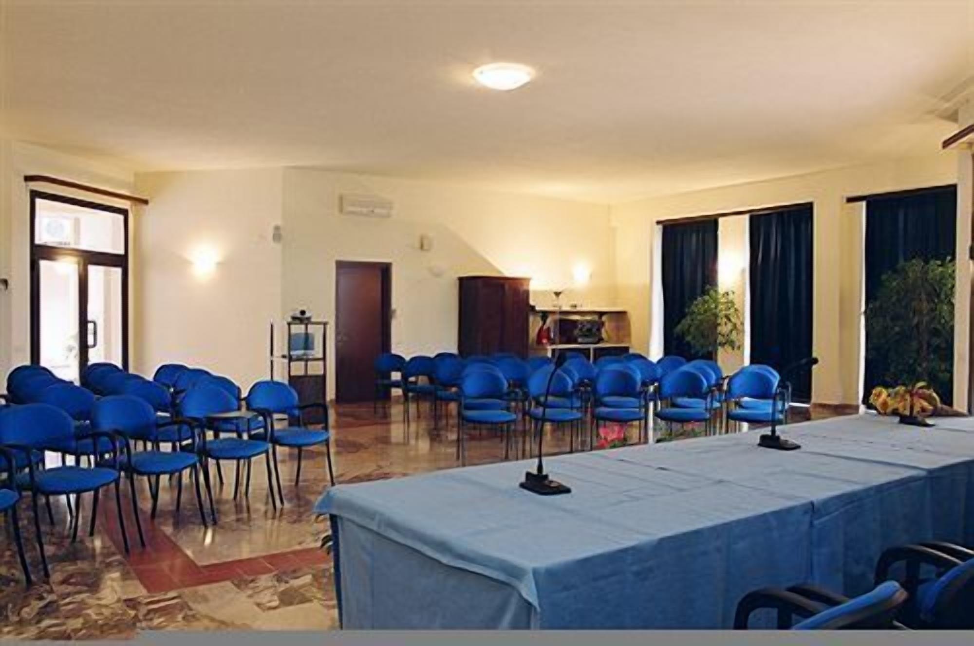 A conference room with rows of blue chairs, a long table covered with a blue tablecloth, and a small stage with a microphone.