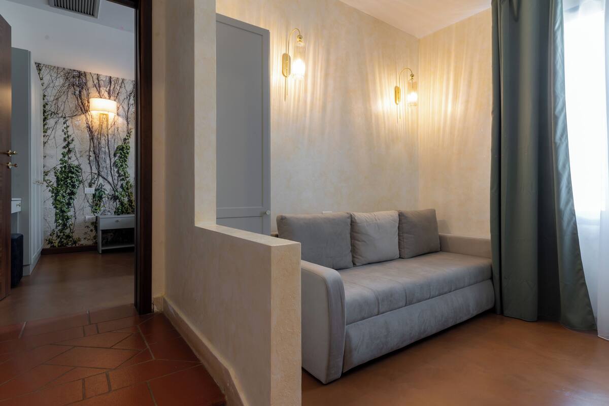 A modern living room with a sofa, a wall-mounted light fixture, and a door leading to another room.