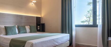 Une chambre d’hôtel avec un lit, une table de chevet, une lampe et une fenêtre avec des rideaux.