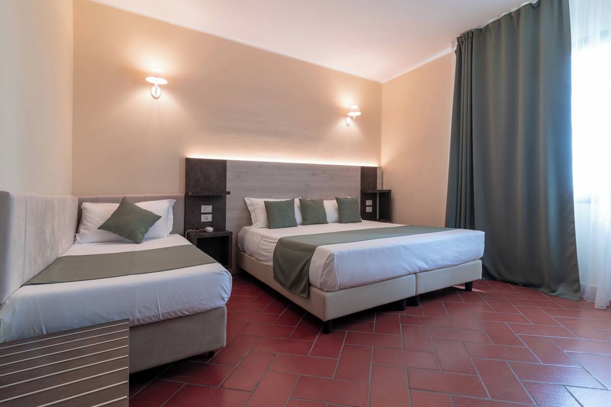 A hotel room with two beds, a sofa, a nightstand, and a wall-mounted light fixture.