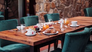 A breakfast table set with plates, glasses, and croissants in a room with stone walls and green chairs. - Hotel Villa Cesi (Impruneta)
