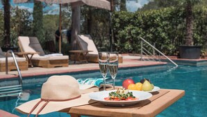 A poolside setting with a table, a hat, a plate of food, and two glasses of water. - Hotel Villa Cesi (Impruneta)