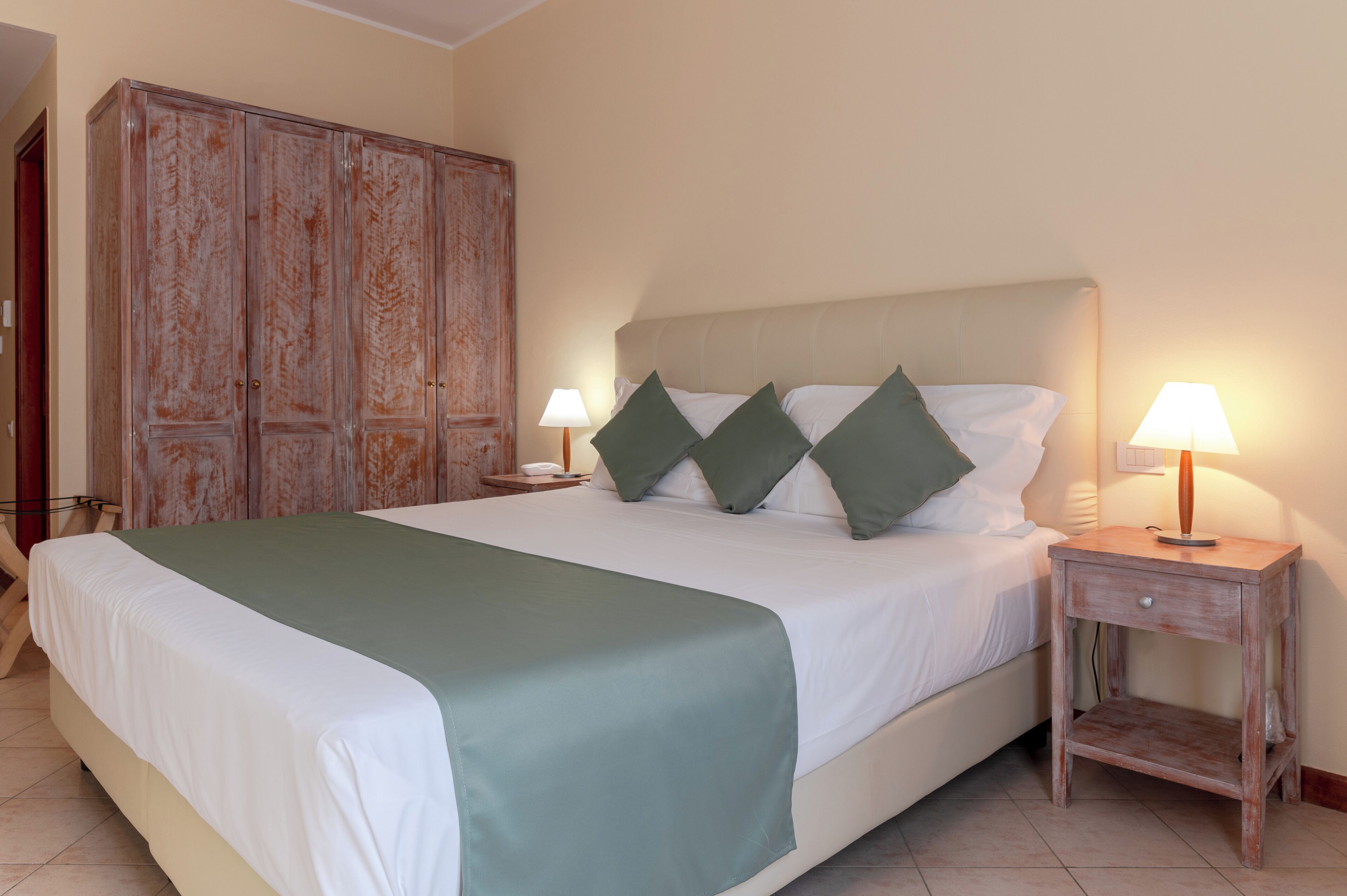 A bedroom with a large bed, two bedside tables with lamps, and a wooden wardrobe.