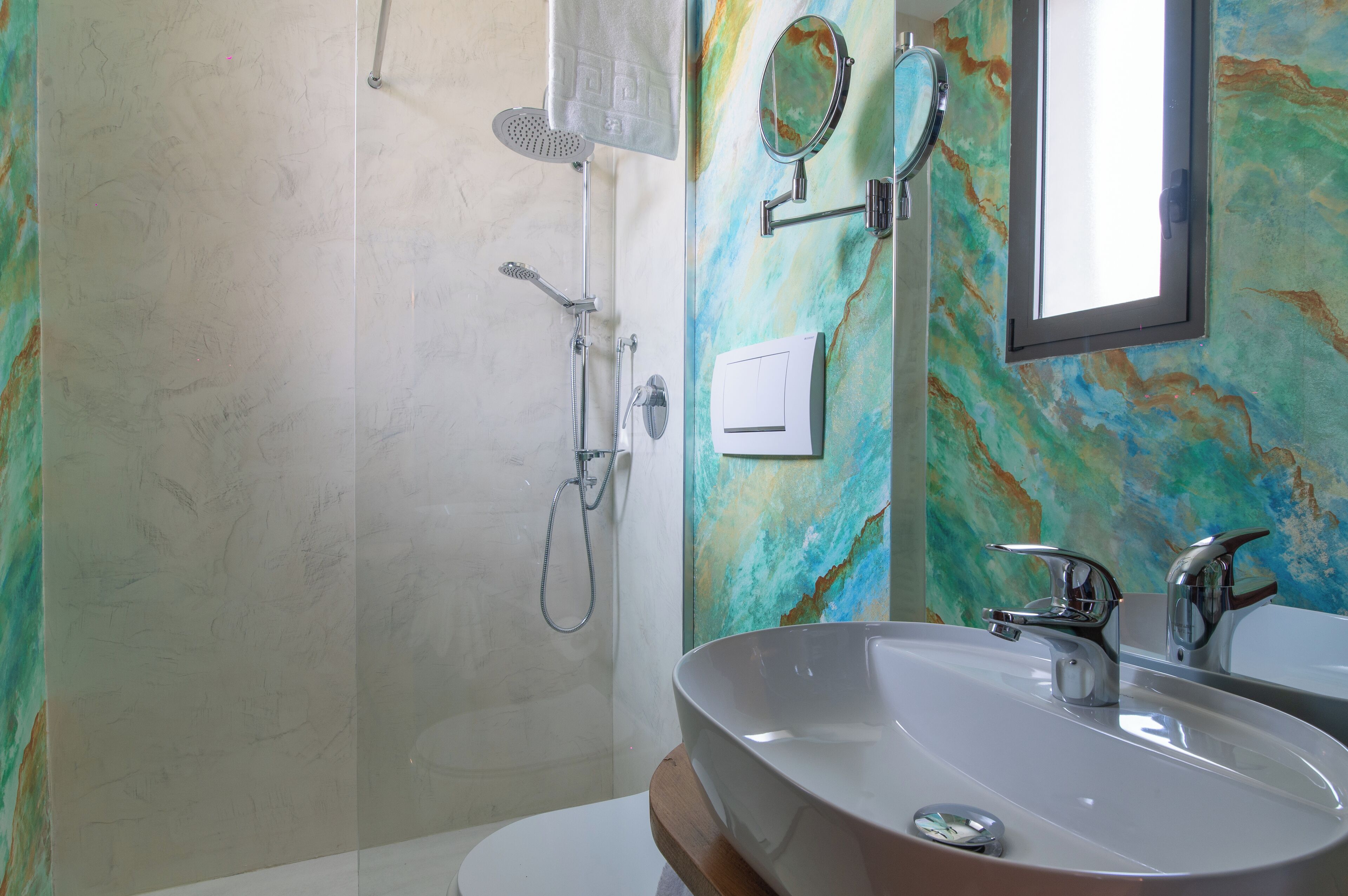 Un baño con un lavamanos grande, ducha, espejo y una pared con un diseño abstracto y colorido.