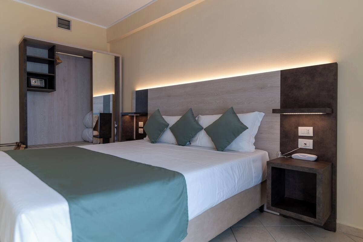 A modern hotel room with a large bed, a bedside table with a phone, and a wardrobe with a mirror.