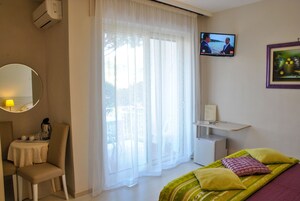 A hotel room with a bed, a TV, a desk with a chair, and a window with sheer curtains.
