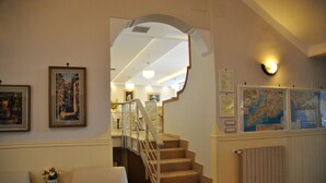 A staircase with a wooden handrail, a white cushioned chair, and a small table with a vase of flowers. - Hotel Villa Fiorita (Sorrento)