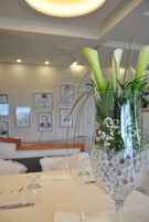 A dining table with a clear glass vase containing white flowers and greenery.
