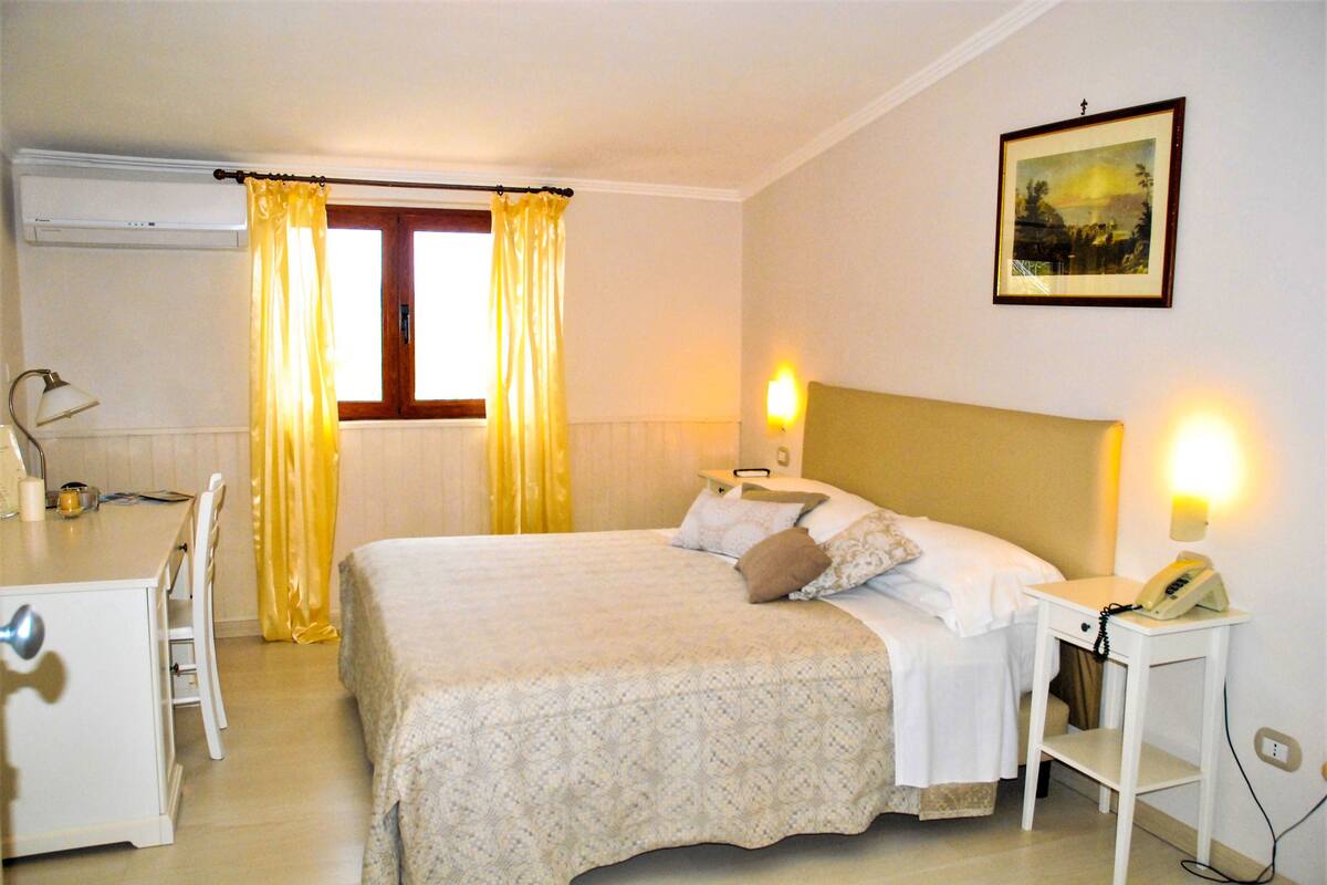 A hotel room with a bed, bedside table, lamp, and a painting on the wall.