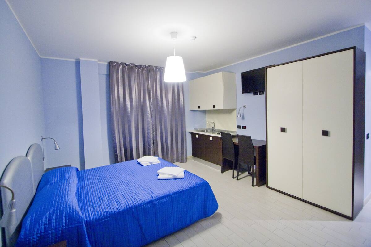 Una camera d'albergo con un letto, una scrivania, una sedia, un armadio e un bagno.