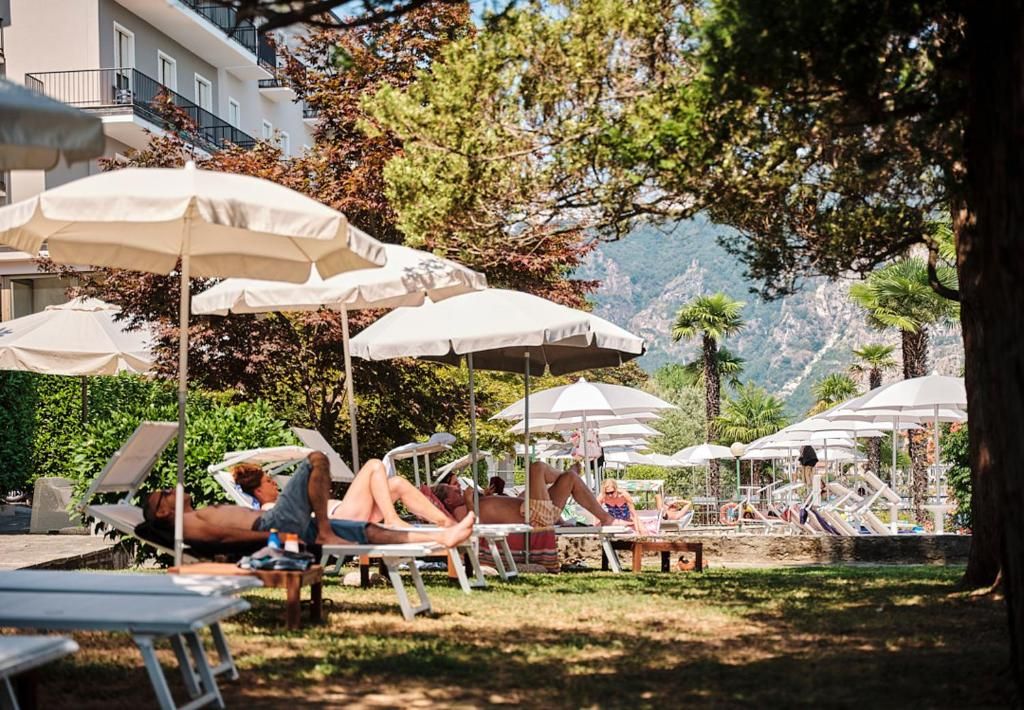 Ein Poolbereich mit Liegestühlen und Sonnenschirmen, umgeben von Bäumen und einer Bergkulisse.