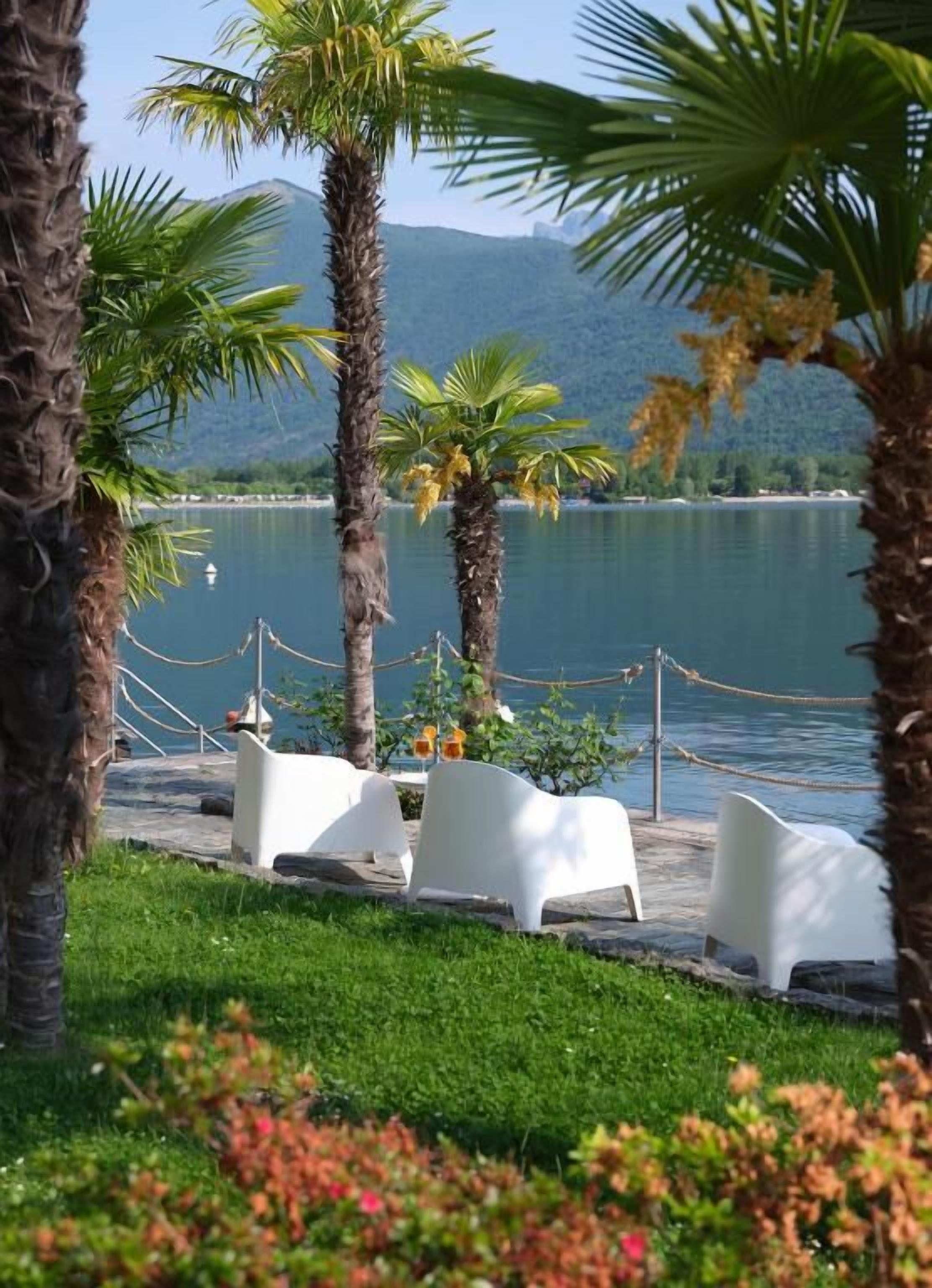 Un entorno tranquilo junto al lago, con palmeras, sillas de descanso blancas y una vista despejada del agua.