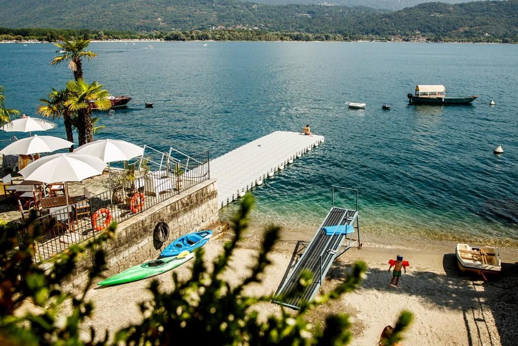 Vista del lago con muelle, barcos y una playa con sombrillas y un kayak.