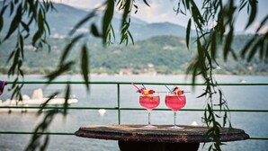 Two red cocktails on a rustic table with a view of a lake and mountains in the background. - Hotel Carillon (Baveno)
