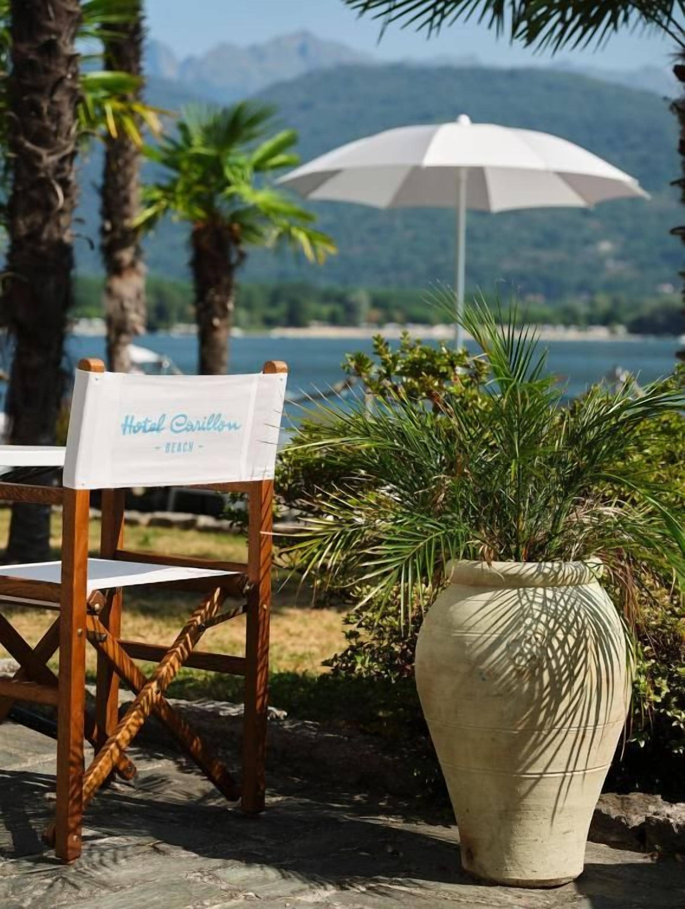 A chair with a sign reading 'Hotel Carillon - Beach' and a large potted plant with a white umbrella in the background.