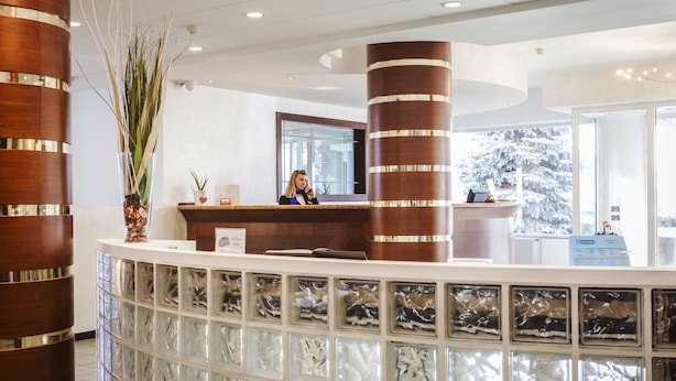 A reception area with a wooden reception desk, a large mirror, and a glass display case with decorative items. - Hotel Donizetti (Lallio)