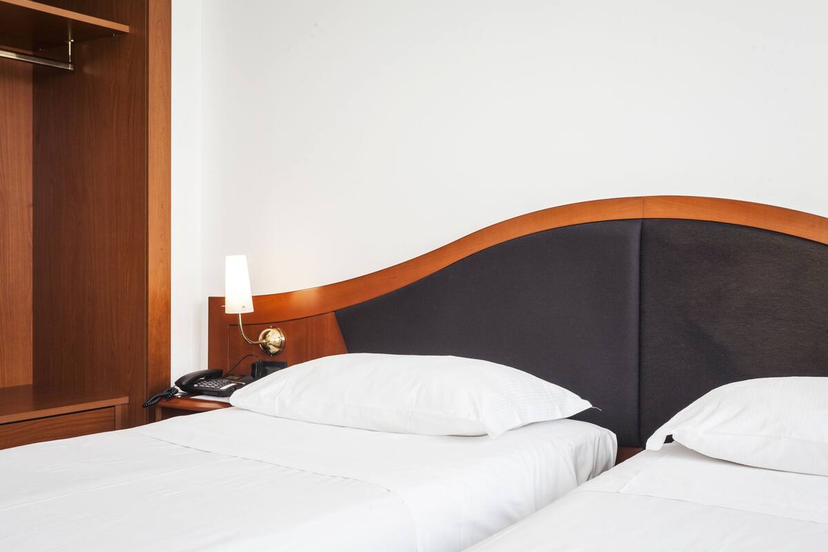A hotel room with two beds, a wooden wardrobe, a bedside table with a lamp, and a telephone.