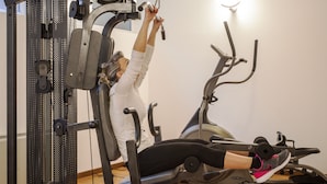 A person using a stationary exercise machine with a weight stack and handles. - Hotel Donizetti (Lallio)
