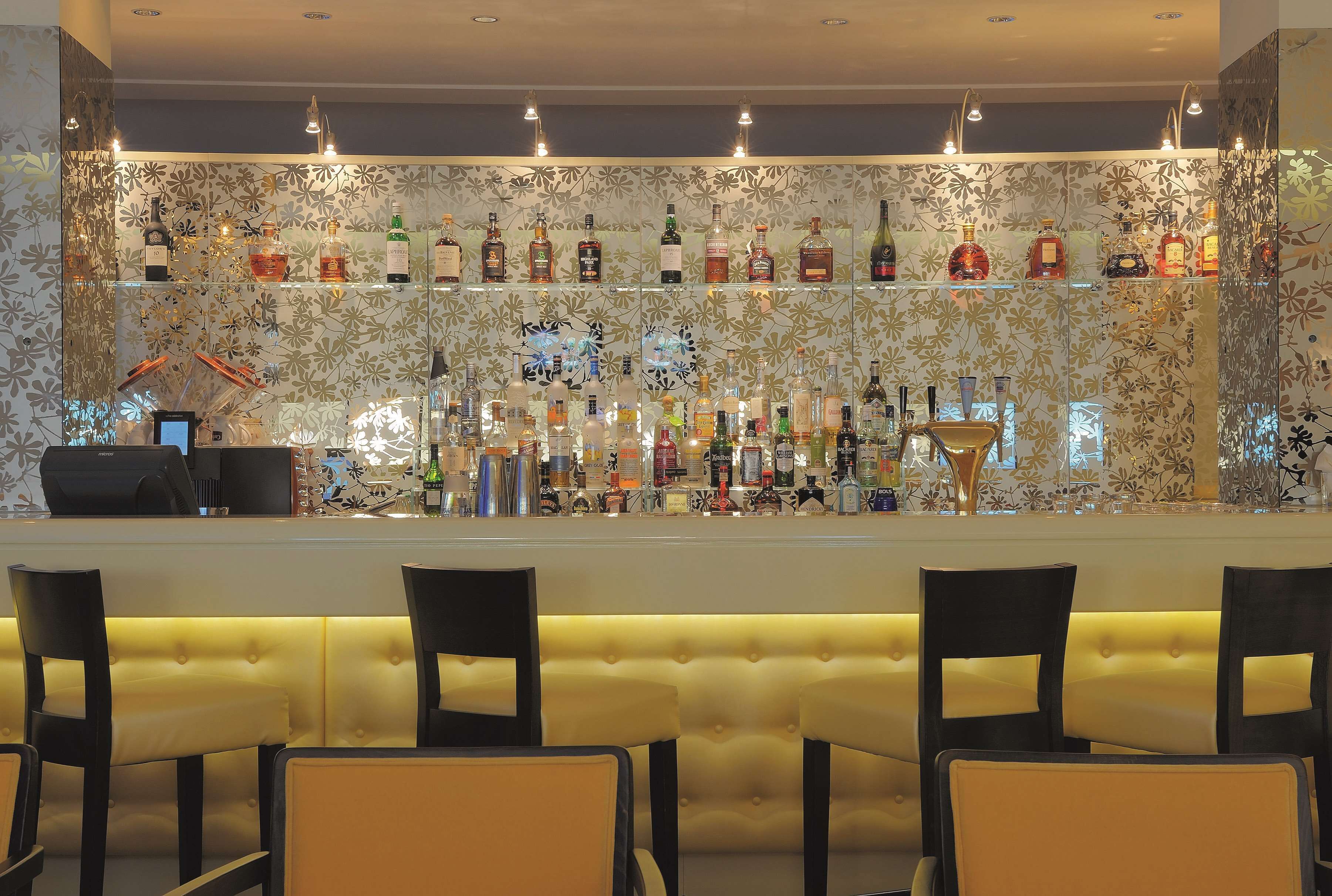 A bar area with multiple shelves of liquor bottles, a cash register, and several chairs.