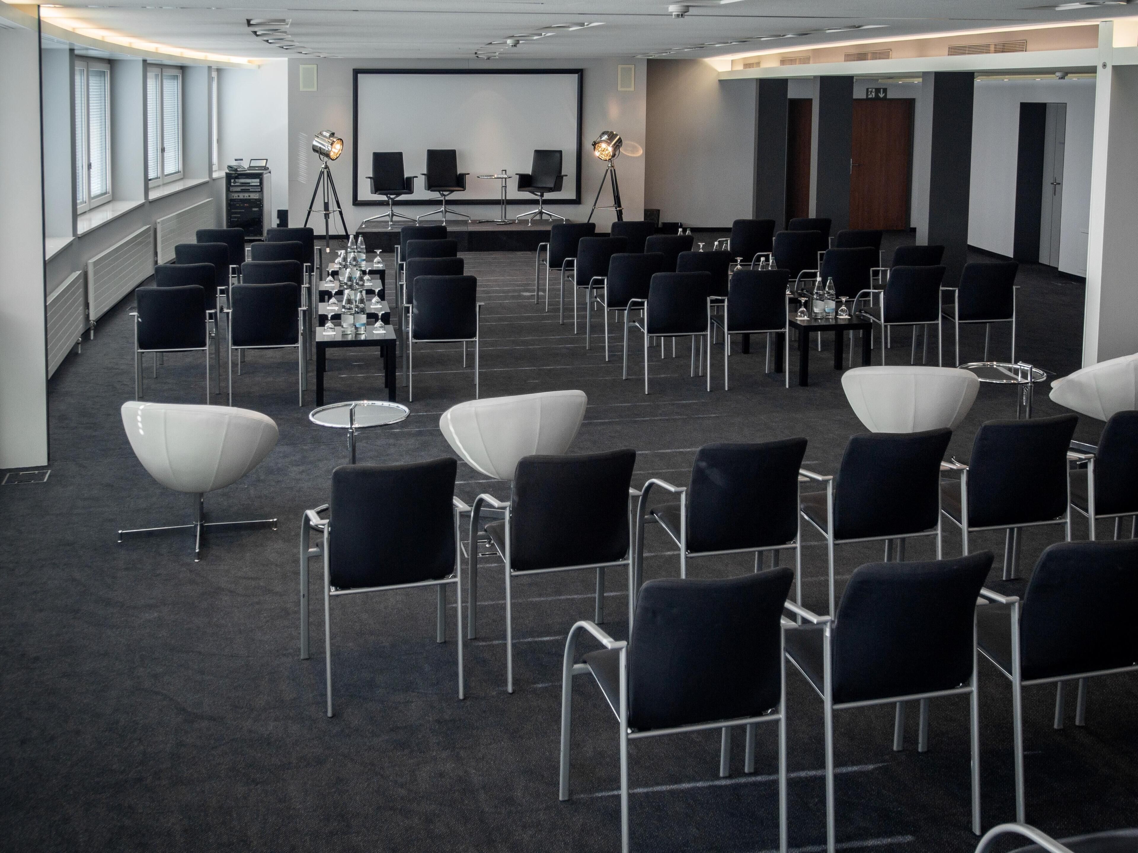 A conference room with rows of chairs, a projector screen, and tables with water bottles.