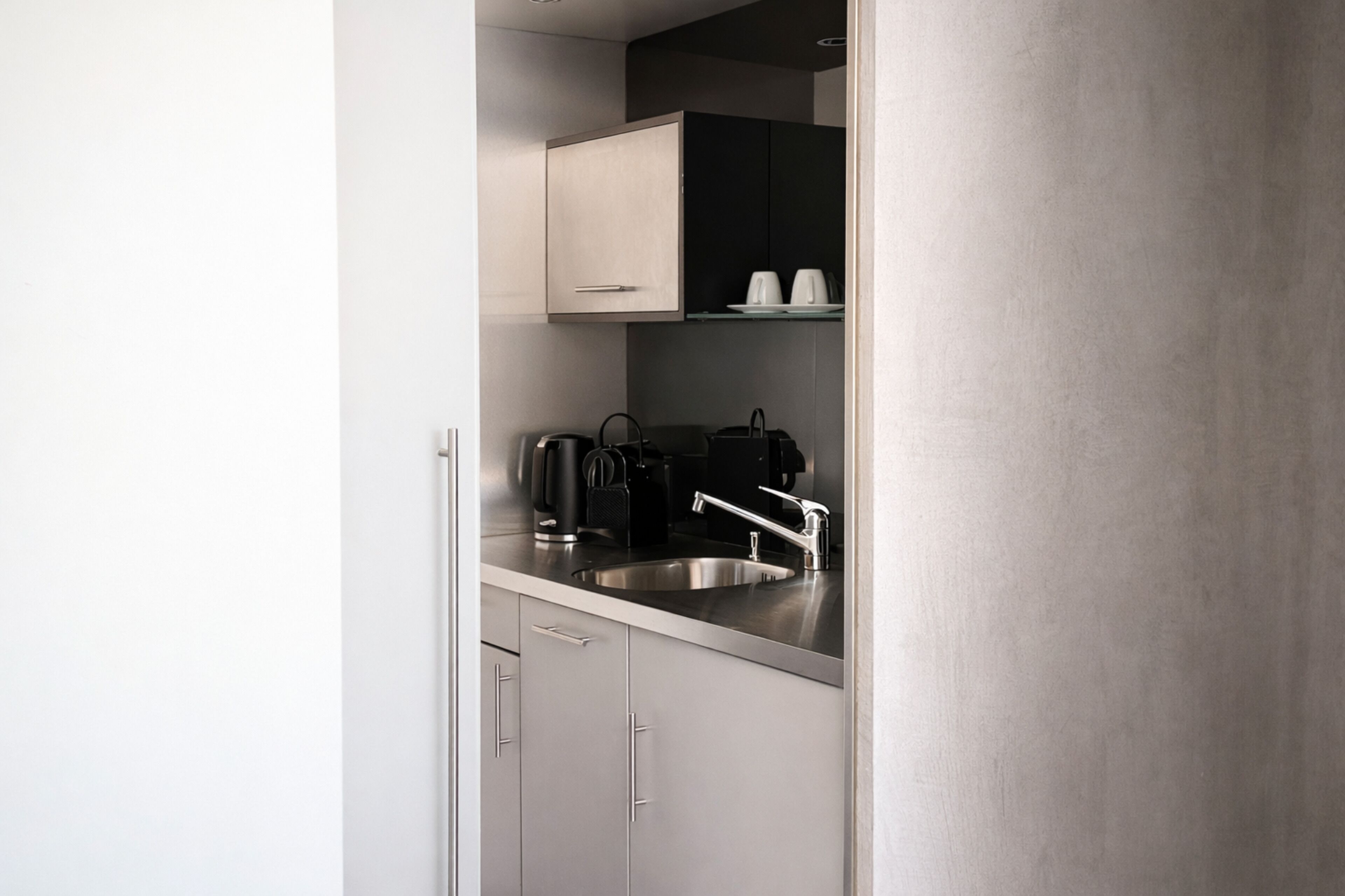 A modern kitchen with a stainless steel sink, a kettle, and a coffee maker.