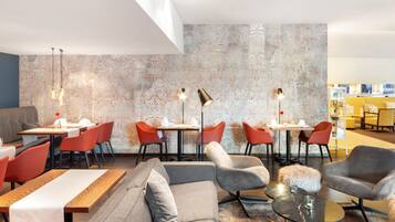 Un espace repas moderne avec des tables hautes, des chaises rouges et un canapé gris.
