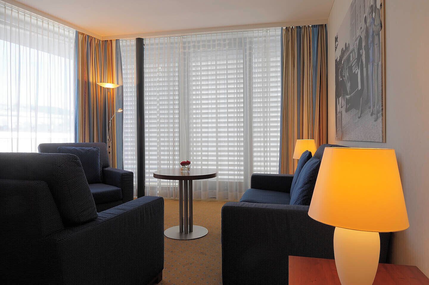 A hotel room with two sofas, a small round table, and a lamp.