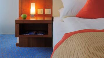 Ein Hotelzimmer mit Nachttisch aus Holz, einer Lampe, einem grünen Apfel und einem Bett mit weißen und roten Kissen.