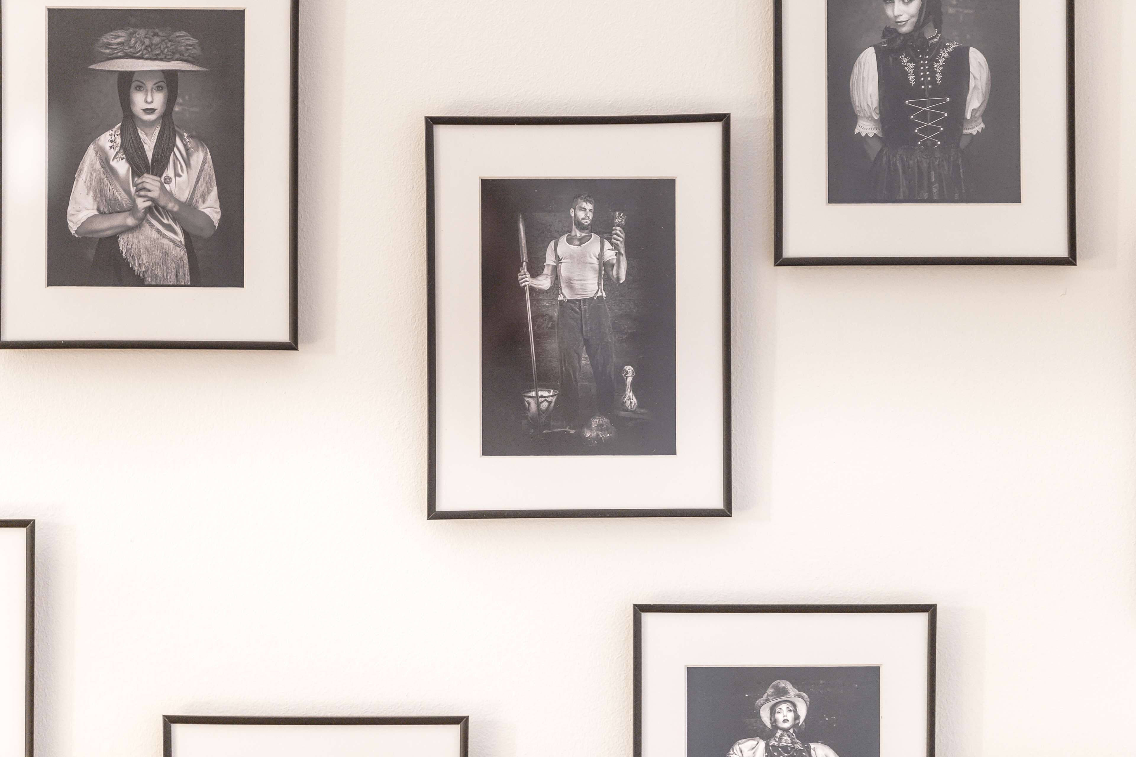 A wall with multiple framed black and white photographs of people in various poses and attire.