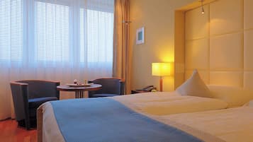 A hotel room with two beds, a small table with a plate of food, a chair, a lamp, and a window with curtains.