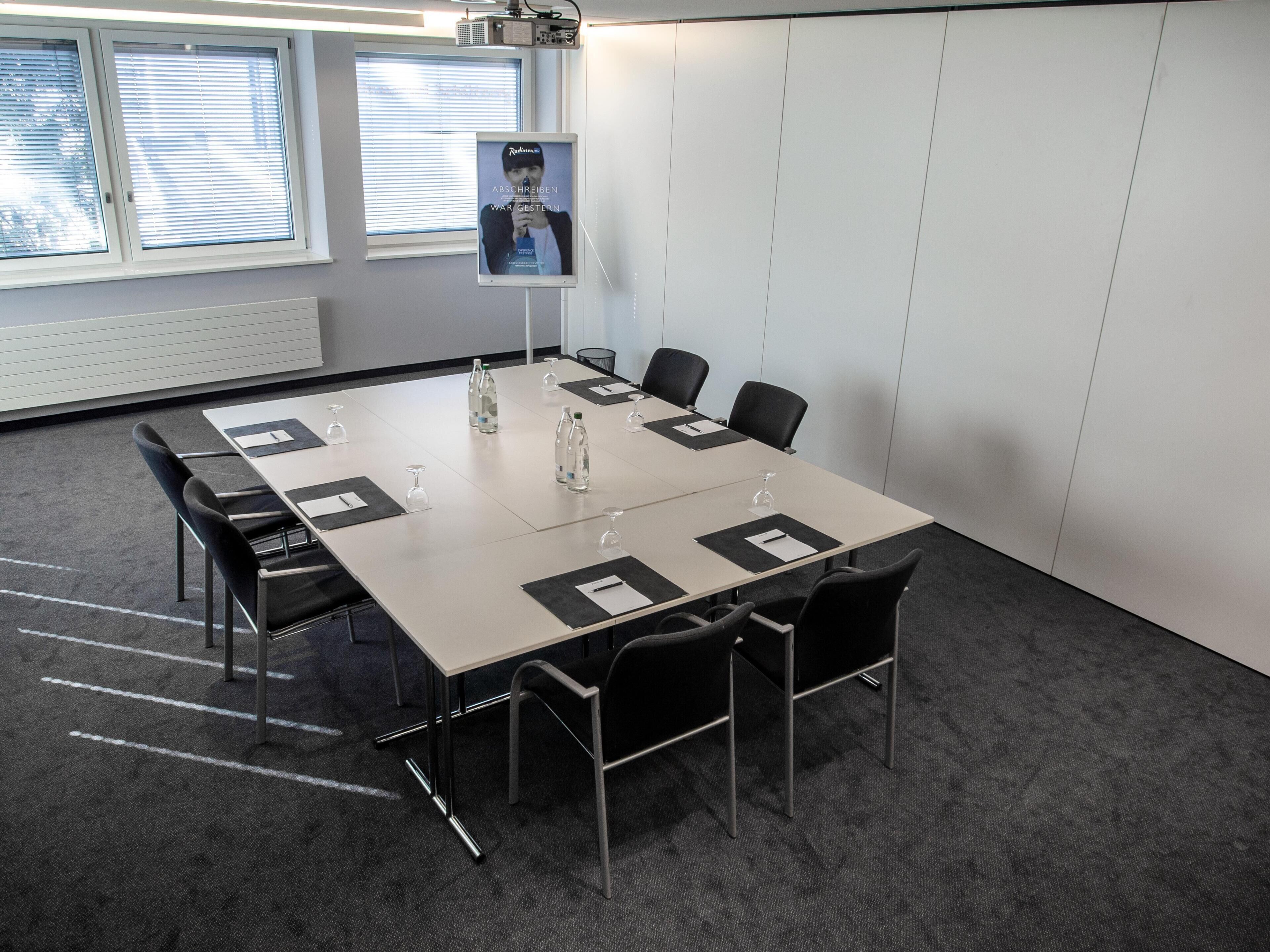 A conference room with a long table, chairs, water bottles, and a poster on the wall.