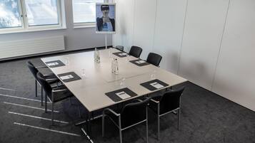 Un salón de conferencias con una larga mesa, sillas, botellas de agua y un cartel en la pared.
