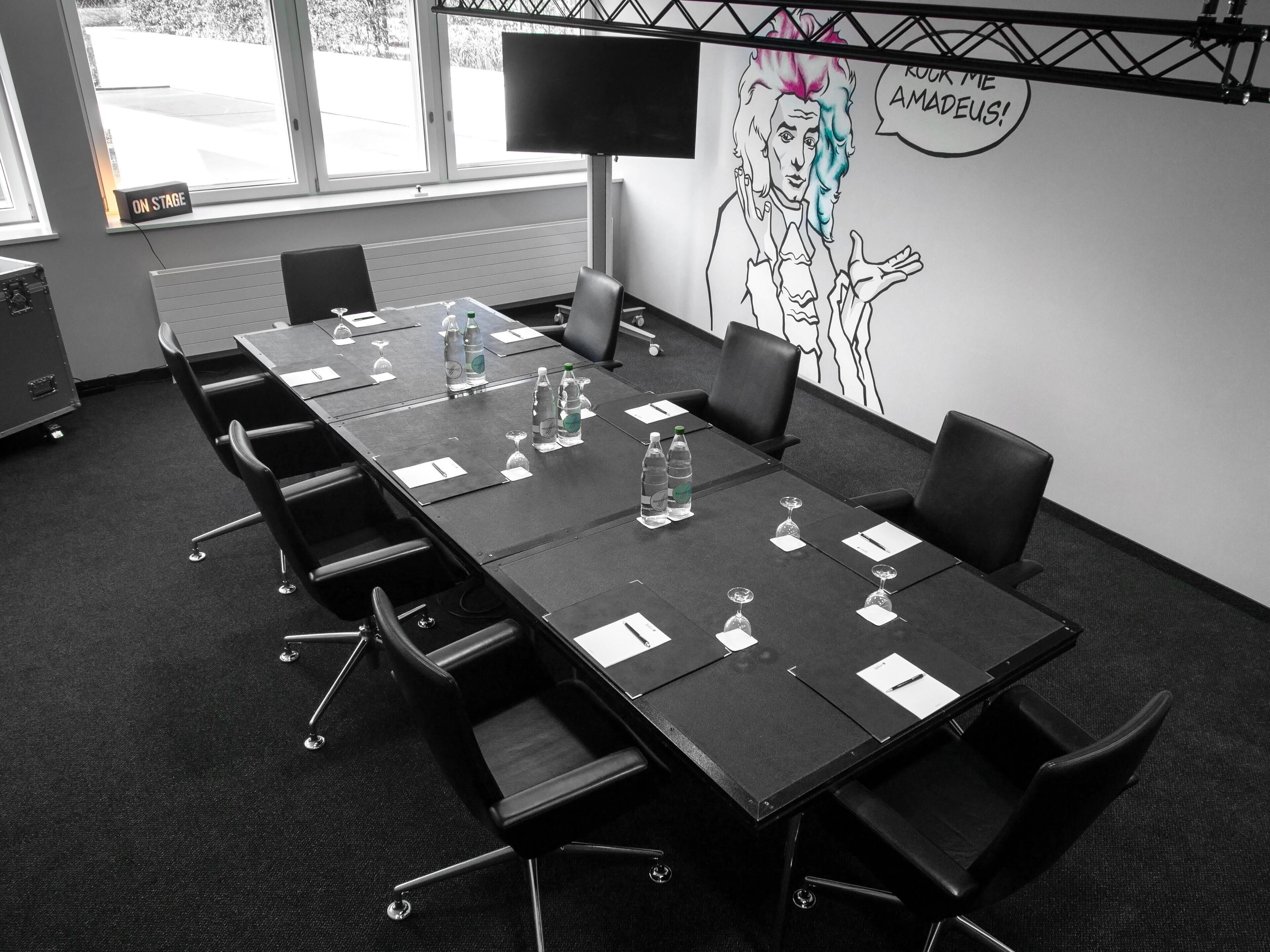 Ein Konferenzraum mit einem langen Tisch, Stühlen, Wasserflaschen und einem großen Bildschirm.
