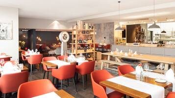 Ein modernes Restaurantambiente mit roten Stühlen, Holztischen und einer Bar.