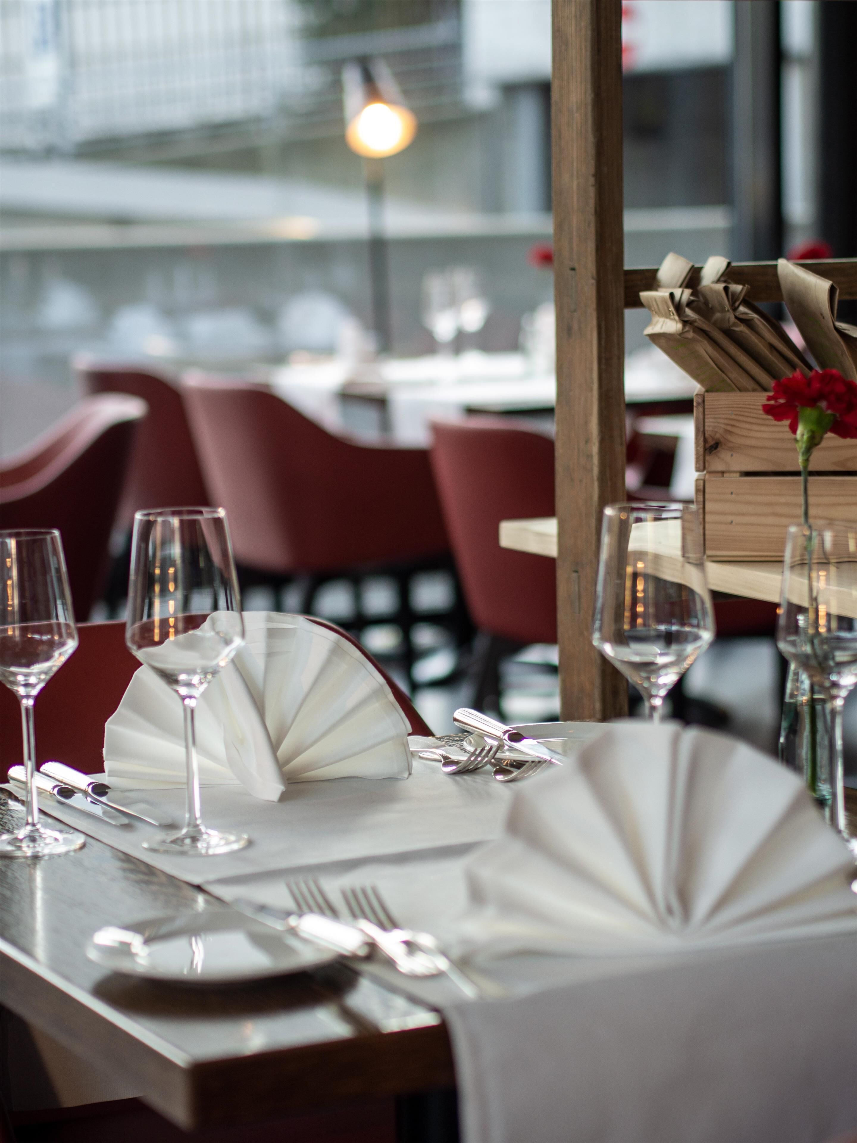 Una mesa de comedor dispuesta con copas de vino, cubiertos y un centro de mesa con una flor roja.