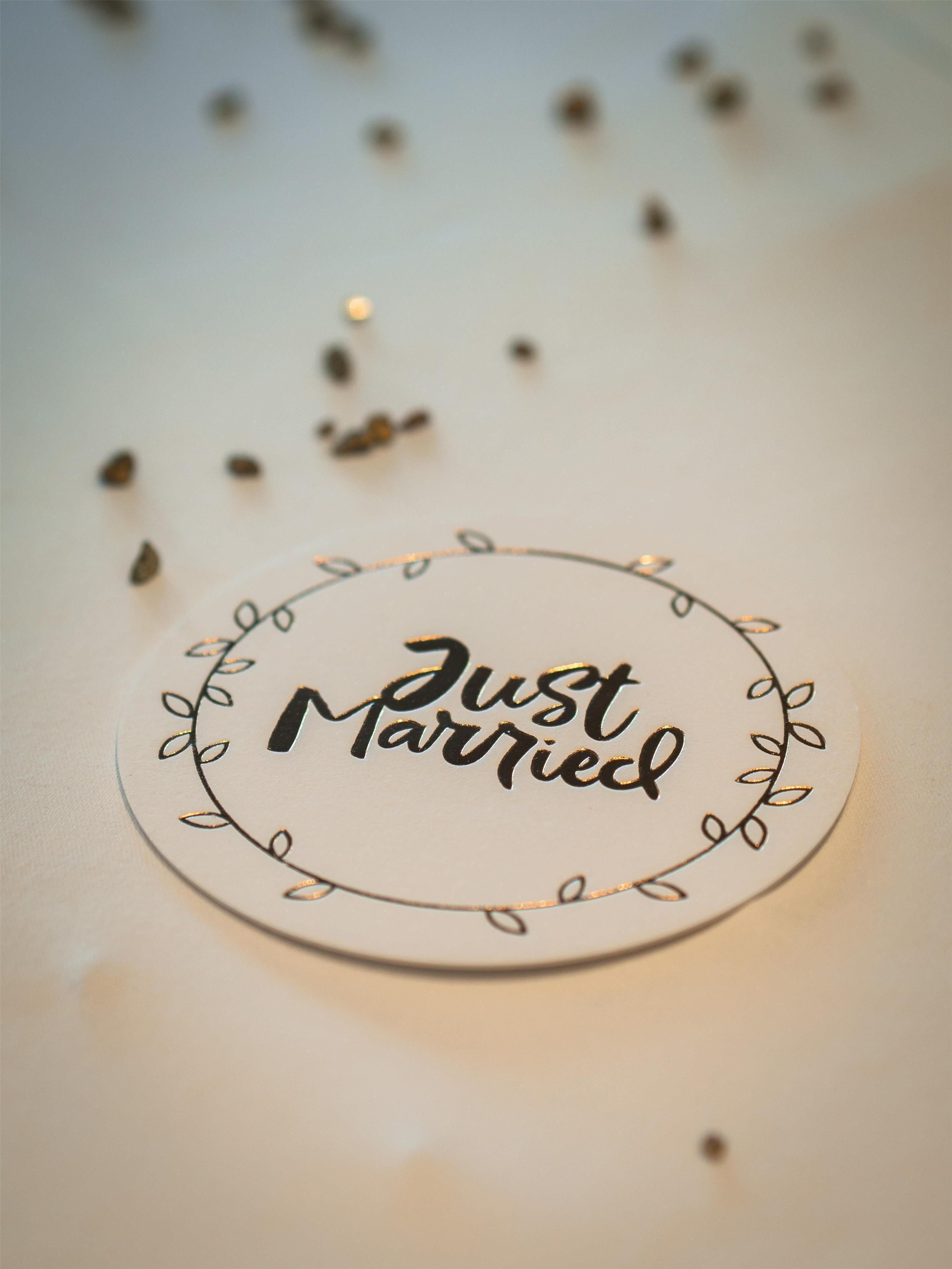 Een rond bord met de tekst 'Just Married', omringd door een decoratief bladmotief.