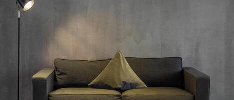 A dark green sofa with a single pillow, a floor lamp, and two framed pictures on the wall.