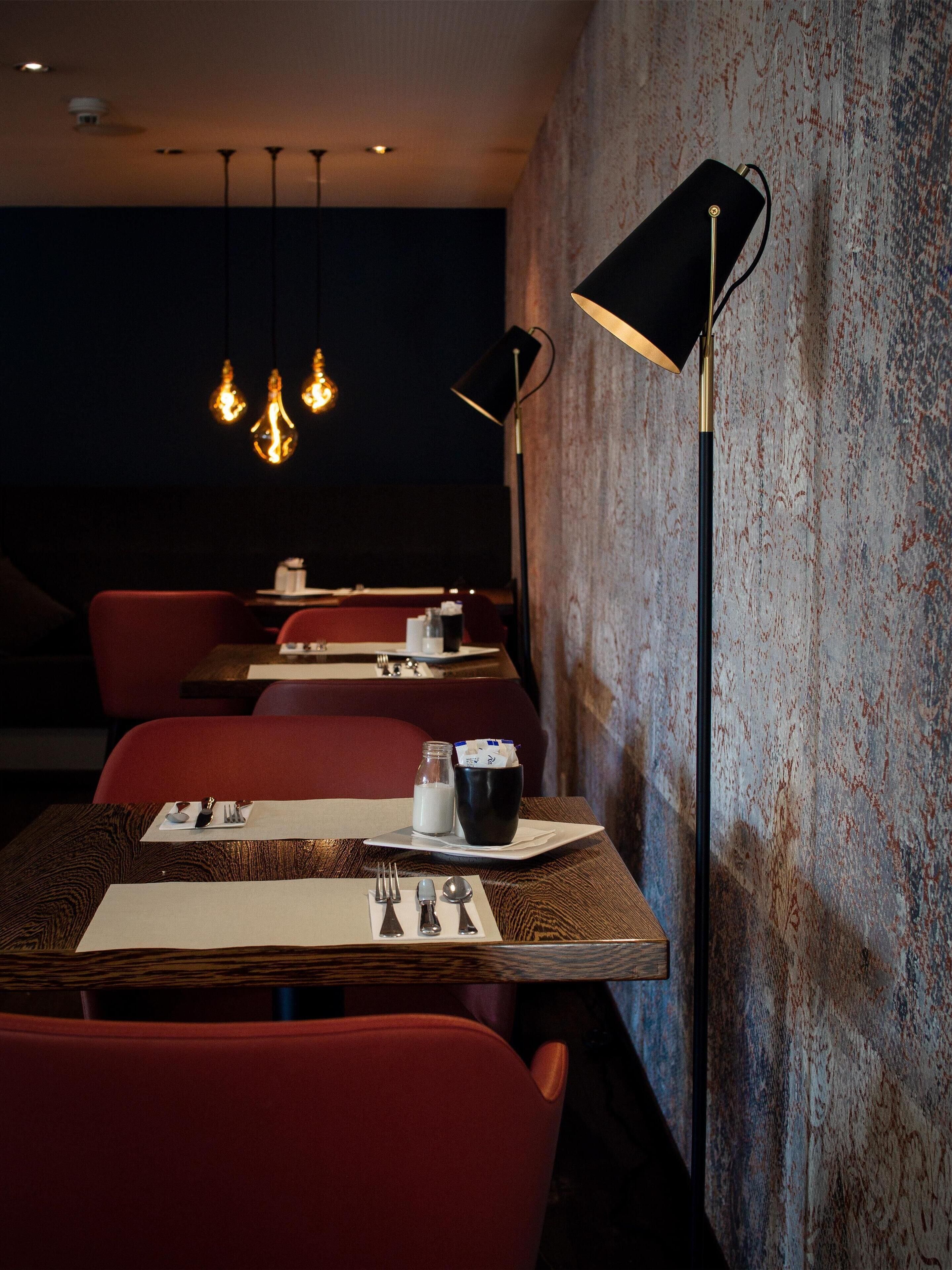 Un interior de restaurante con mesas dispuestas para comer, una lámpara de pie negra y luminarias colgantes.