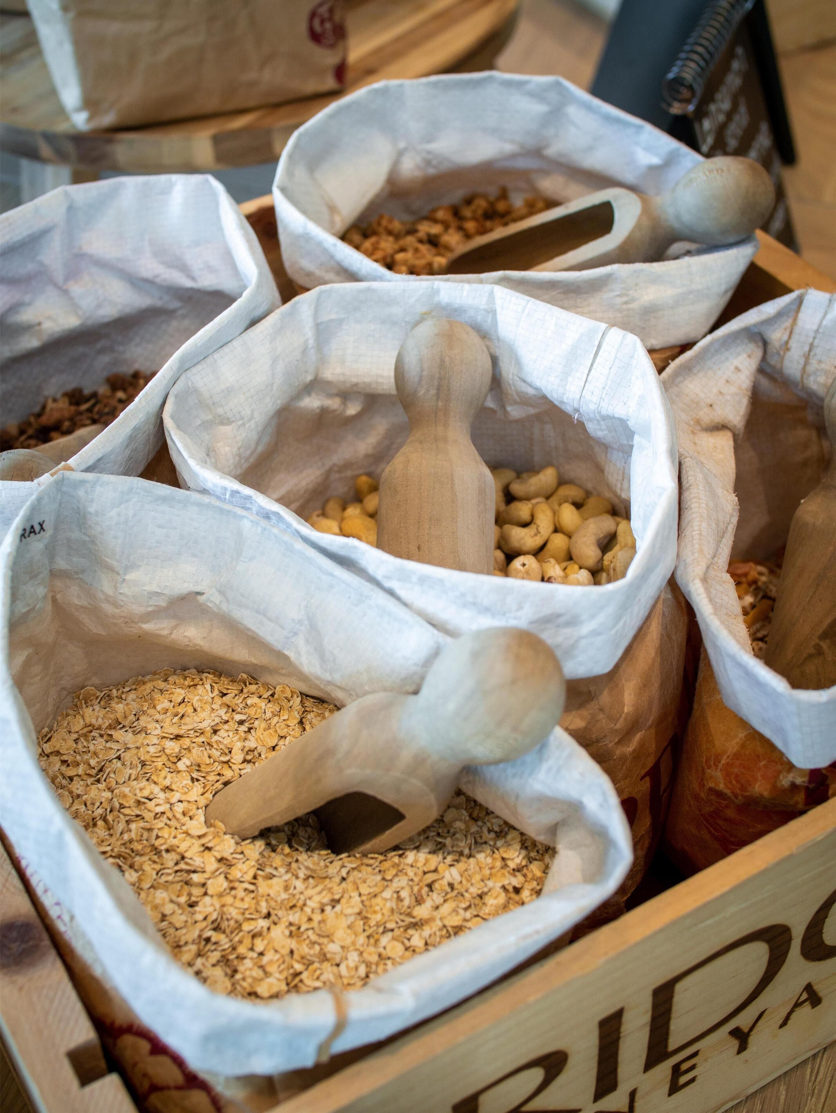 A wooden crate filled with bags containing various grains and legumes, with wooden scoops inside some bags.